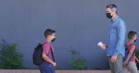 Teacher checking student's temperature at school entrance during covid-19