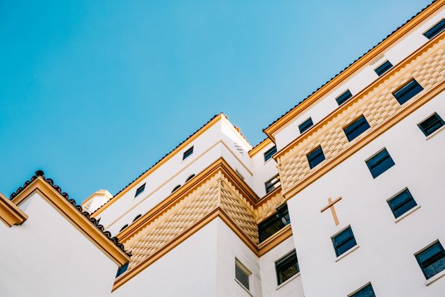 Low-angle view of a white stucco building juxtaposed against a clear blue sky, showcasing its modern architecture with clean lines and geometric shapes. Ideal for use in articles about urban development, architectural design, commercial real estate, or modern cityscapes.
