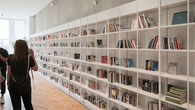 Contemporary minimalist library with tall white modular bookshelves, visitors browsing in daylight