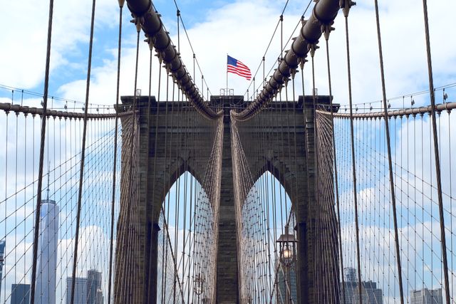 Brooklyn Bridge captured prominently with an American flag on a clear day, reflecting its historic and architectural significance. Great for use in travel brochures, educational materials, tourism websites, and articles on iconic structures in New York City.