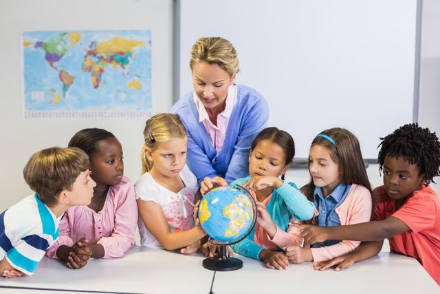 Teacher discussing globe with kids in classroom at school