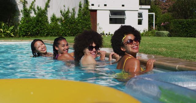 Diverse group of female friends standing at the poolside looking at the camera. hanging out and relaxing outdoors in summer.