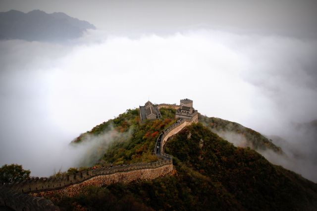 Great Wall of China winding through mist-covered mountains with overcast sky. Useful for travel blogs, tourism advertisements, historical articles, and nature-focused content.