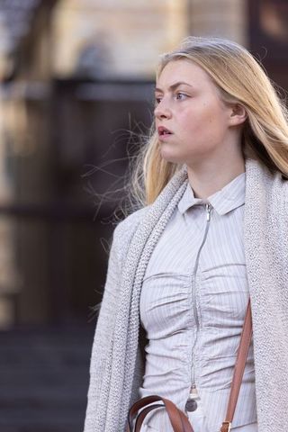 Young woman standing on urban steps wearing cardigan and zippered blouse, looking sideways
