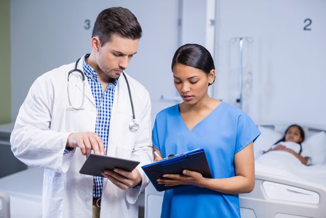Doctor and nurse using digital tablet and clipboard in hospital room