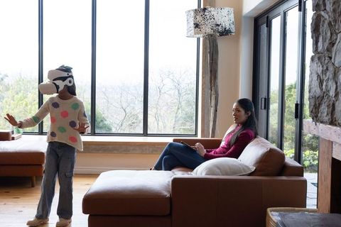 Child exploring virtual reality while parent relaxing on modern rustic living room sofa