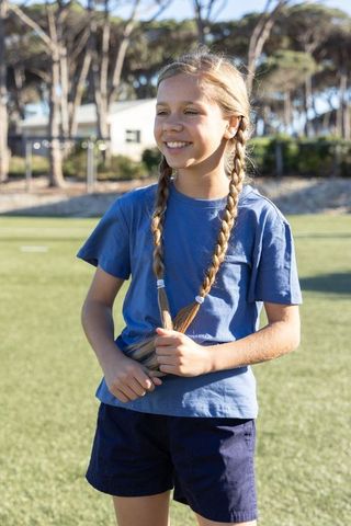 Preteen girl smiling on sunny sports field holding braided pigtails in blue shirt