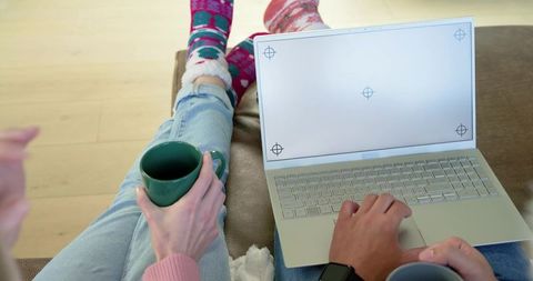 Couple relaxing on sofa using laptop and holding mugs, cozy morning at home