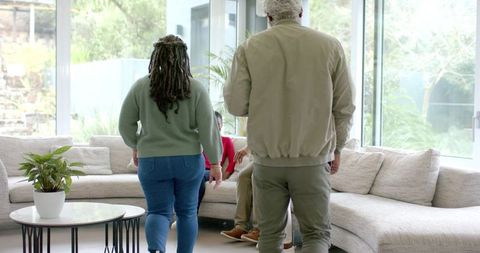 Diverse multigenerational family walking toward curved beige sectional sofa in sunlit living room