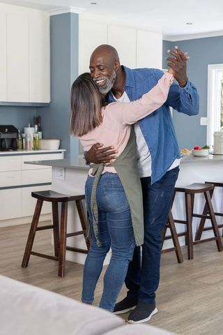Middle-aged african american couple dancing in bright modern kitchen while cooking together
