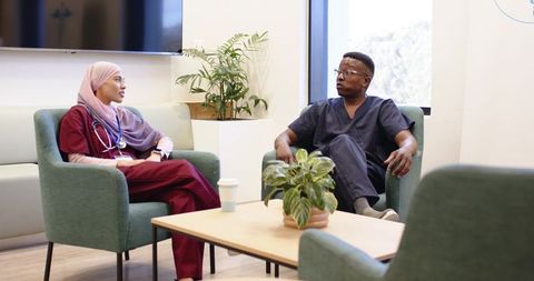 Nurse wearing hijab and clinician in scrubs having conversation in clinic lounge