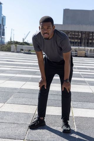 African american runner leaning forward catching breath on urban plaza wearing smartwatch