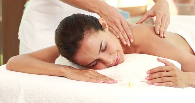 The image depicts a woman lying on a massage table, receiving a professional back massage. This relaxed and content atmosphere is perfect for advertisements and content related to spa services, wellness, therapy, and health. Ideal for promoting massage parlors, wellness retreats, and rejuvenation treatments.