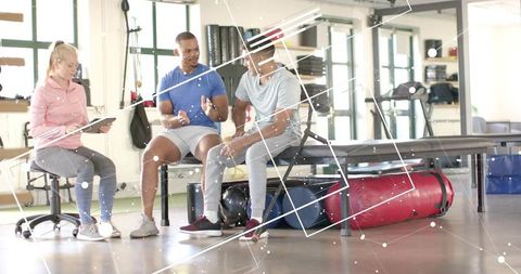 Physical therapist consulting two clients on rehab exercises using tablet in daylight gym