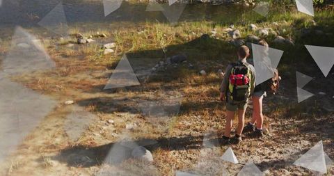 Young couple hiking by riverside with backpacks and boots, sunlit trail and shadows