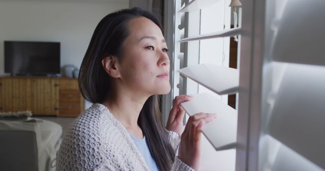 Pensive Woman Looking Through Window Blinds in Living Room - Download Free Stock Images Pikwizard.com