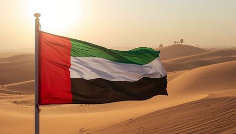 United arab emirates flag waving over sunlit desert dunes at golden hour