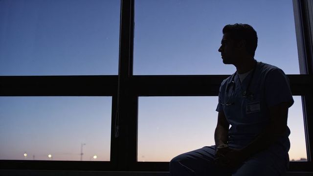 Silhouetted doctor gazing out window at twilight, contemplative healthcare portrait