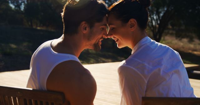 A young Caucasian couple shares a tender moment, gazing into each other's eyes with affection, with copy space. Their intimate connection is highlighted by the warm sunlight that envelops them, creating a romantic and serene atmosphere.