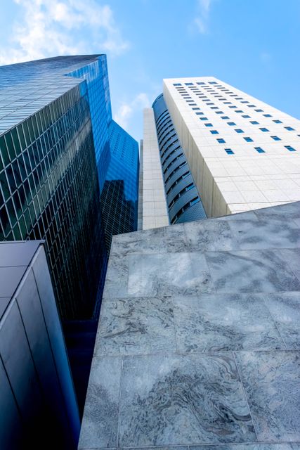 Photo shows a group of modern skyscrapers and office buildings reaching into a clear blue sky. Glass facades and concrete walls create a sharp and sleek aesthetic. Ideal for use in business and corporate publications, real estate promotions, and articles about urban development or architecture.