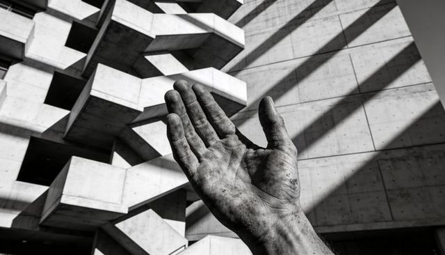 Reaching Dirty Callused Hand Toward Brutalist Concrete Geometry Under Strong Diagonal Light