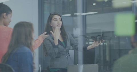 Businesswoman presenting quadcopter in glass office while team discussing drone strategy