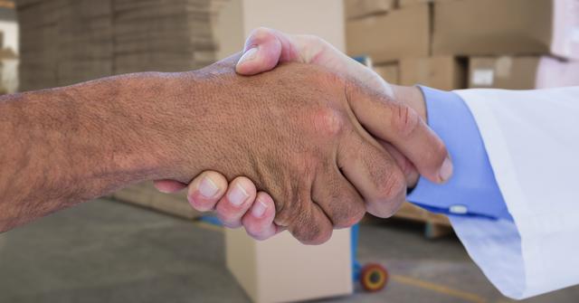 Close-up view of two individuals shaking hands within a warehouse, symbolizing business agreement, partnership, and collaboration. This image can be effectively used for materials on business deals, teamwork in logistics, trust building, and partnership confirmations.