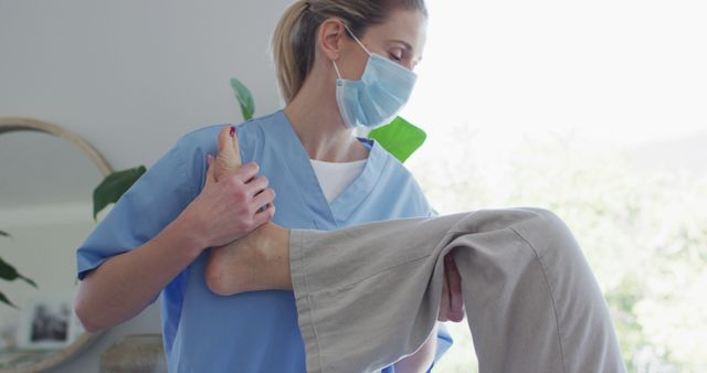 The image shows a physiotherapist wearing a medical mask, providing physical therapy to a patient, likely guiding leg exercises. This image can be used in materials related to healthcare services, physical therapy practices, wellness centers, or articles about rehabilitation and recovery.