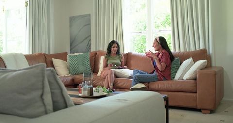 Multiethnic friends chatting on tan leather sectional in sunlit modern living room