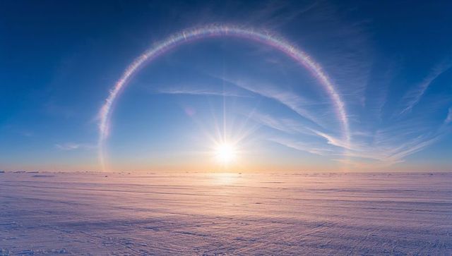 Glowing sun halo rising over frozen arctic plain with rainbow circumzenithal arc at sunrise
