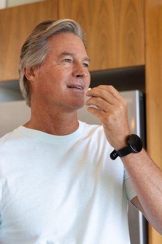 Mature man taking supplement in modern kitchen wearing black smartwatch, healthy lifestyle