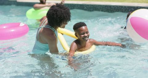 Mother Teaching Son to Swim with Noodle Float in Sunny Pool