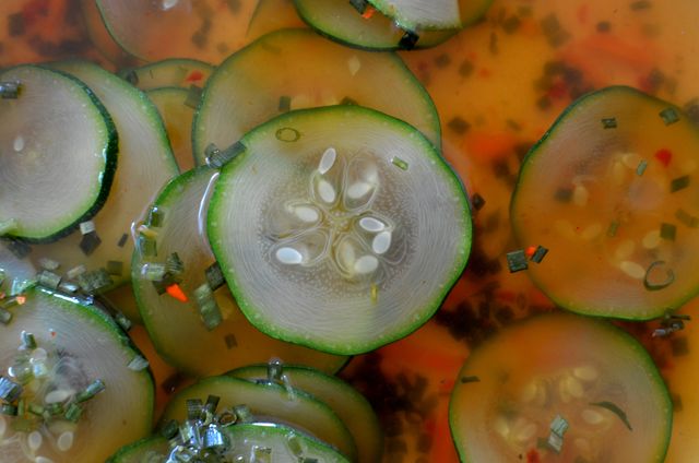 Close-up image showcasing fresh zucchini slices immersed in flavorful broth with visible herbs and spices. Ideal for use in culinary blogs, healthy eating articles, or food-related promotions highlighting fresh ingredients and vegetable-based dishes.