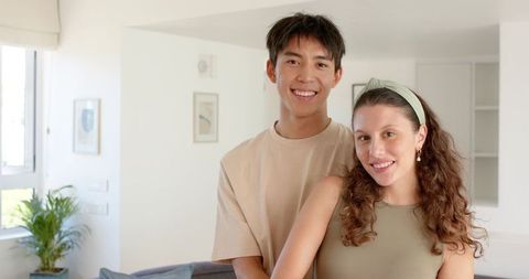 Smiling diverse young couple embracing in bright minimalist living room, home togetherness