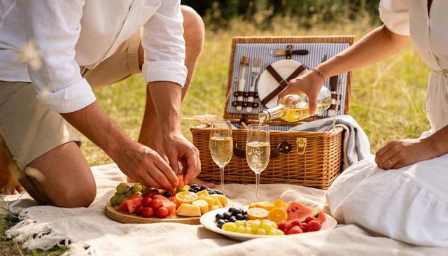 Couple pouring white wine during romantic picnic on blanket in sunlit meadow