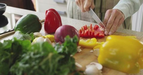 Senior woman chopping colorful bell peppers on wooden board for healthy home cooking