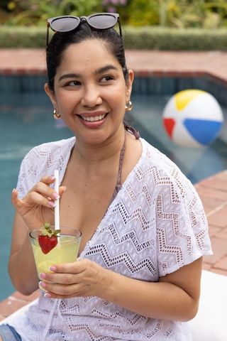 Smiling woman relaxing poolside in white lace cover-up sipping lemon drink with strawberry