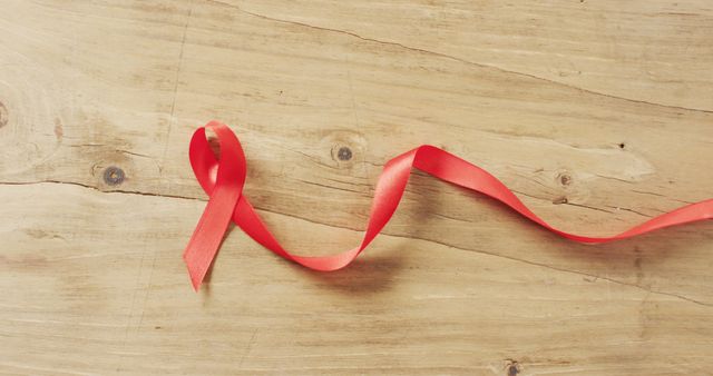 Red ribbon symbolizing awareness of HIV/AIDS placed on wooden background. Ideal for usage in articles, campaigns, social media shares, health awareness posts, and educational content emphasizing support and solidarity.