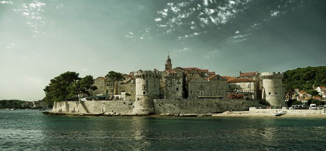 View of a medieval coastal town featuring fortified stone walls and historic buildings along the waterfront. The image captures the charm and antiquity of the village, making it ideal for use in travel brochures, history documentaries, and tourism websites. Perfect for showcasing European heritage and seaside beauty.