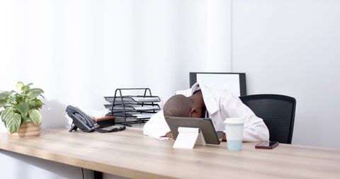 African american doctor resting head on arms at desk in bright minimalist office