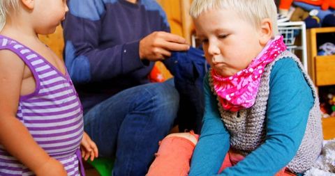 Toddler in bedroom dressing with father and sibling playing