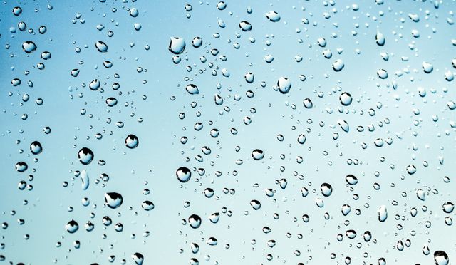 Water droplets on a transparent glass surface with clear sky background. Perfect for illustrating weather conditions, rain effects or natural water formation. Ideal for use in backgrounds, scientific materials or environmental themes.
