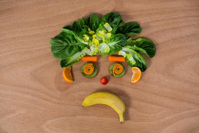 Creative arrangement of fruits and vegetables forming a sad face on a wooden table. Ideal for promoting healthy eating, food art, and creative culinary presentations. Suitable for use in health and wellness blogs, nutrition articles, and educational materials about healthy diets.