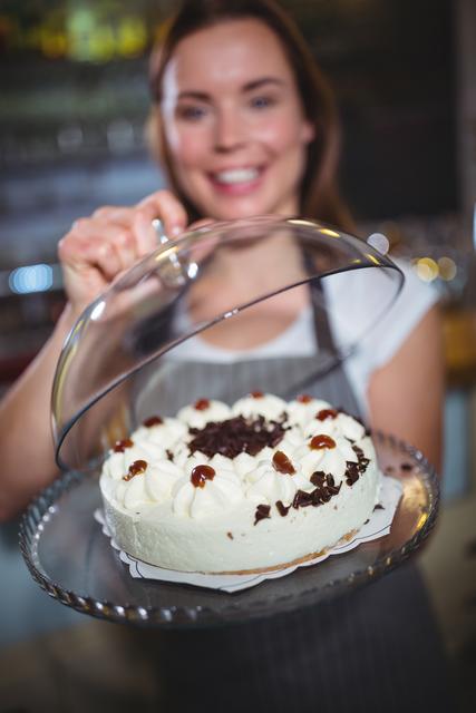 Waitress in a cafe smiling while presenting a delicious cake on a plate. Ideal for use in advertisements for cafes, bakeries, or restaurants. Can be used in marketing materials for hospitality services, food blogs, or culinary magazines.