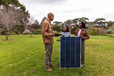 African american family holding solar panel and using tablet in garden discussing solar energy