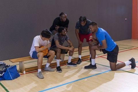 Basketball team huddling on indoor court coach giving strategy to diverse male players
