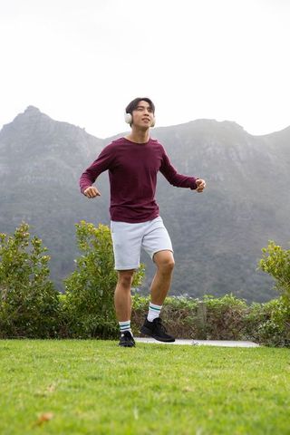 Asian man jogging near mountain ridge wearing white headphones and maroon top