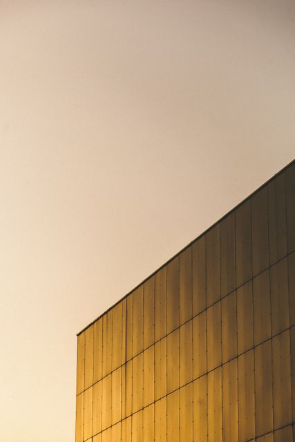 Golden reflections on a modern architectural building facade during sunset create a minimalist urban aesthetic. Ideal for use in architectural design projects, urban development presentations, and as a decorative print to enhance a modern living or office space.