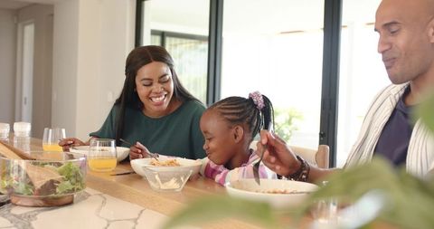 Joyful african american family enjoying breakfast at bright kitchen island with daughter