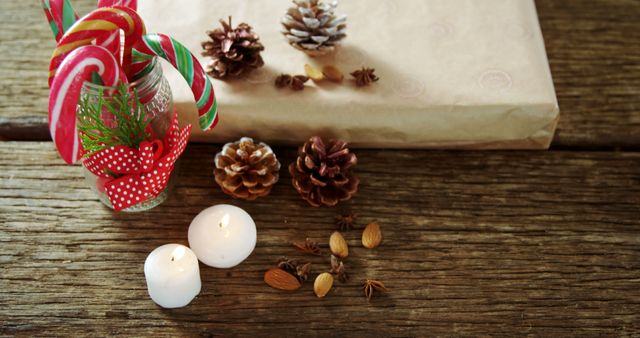 Candy canes, a wrapped gift, and festive decorations create a warm holiday atmosphere, with copy space. Pine cones, lit candles, and spices add a traditional touch to the Christmas-themed composition.